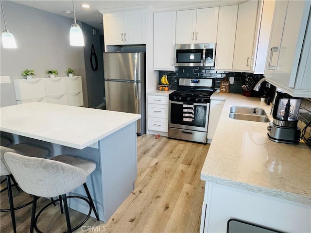 kitchen featuring a sink, stainless steel appliances, light wood-style floors, white cabinetry, and backsplash