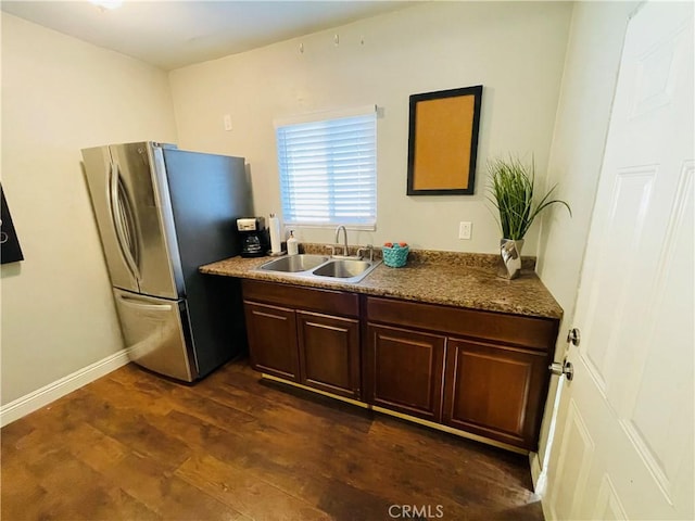 kitchen with dark brown cabinetry, a sink, baseboards, freestanding refrigerator, and dark wood-style floors