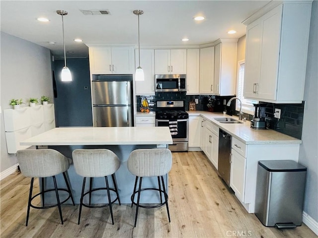 kitchen with sink, appliances with stainless steel finishes, white cabinets, a kitchen island, and decorative light fixtures