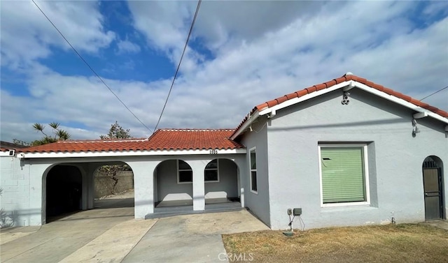 rear view of house featuring covered porch, a tile roof, and stucco siding