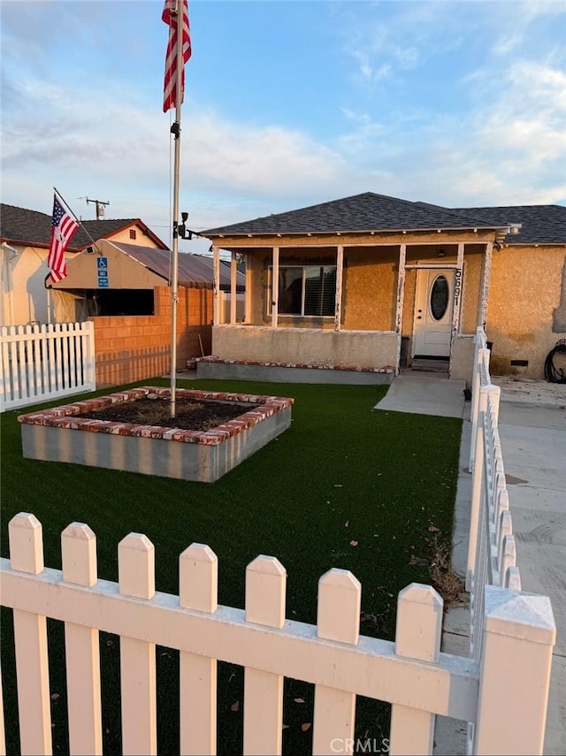 view of front of property with a shingled roof, a front yard, fence, and stucco siding