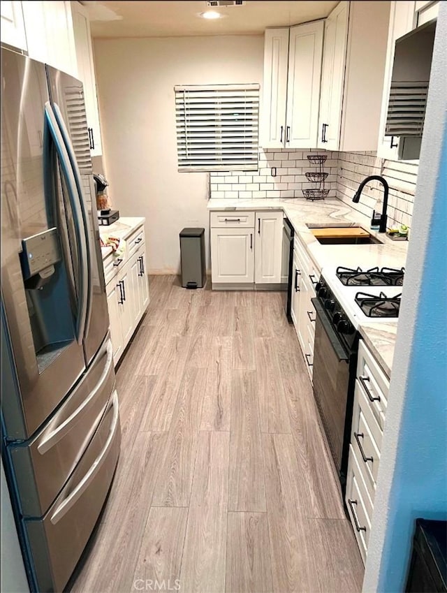 kitchen featuring a sink, light wood-type flooring, dishwasher, gas stove, and stainless steel fridge