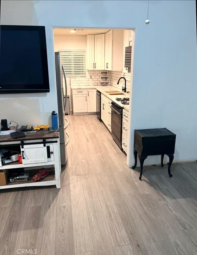 kitchen with sink, backsplash, range with gas stovetop, and light hardwood / wood-style floors