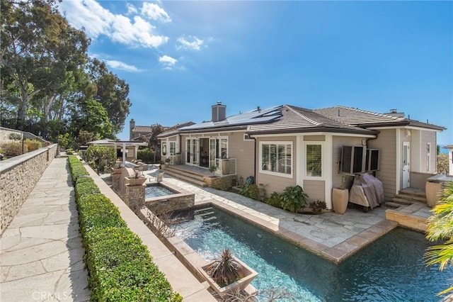 rear view of property featuring a fenced in pool, a patio area, and solar panels