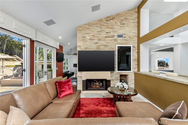 living room featuring ceiling fan, lofted ceiling, and a stone fireplace