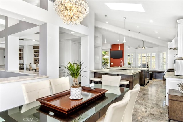 dining room featuring sink, ceiling fan with notable chandelier, a skylight, and high vaulted ceiling