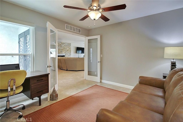 tiled home office with a fireplace, french doors, and ceiling fan