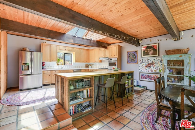 kitchen with appliances with stainless steel finishes, a breakfast bar, a skylight, light brown cabinets, and beam ceiling