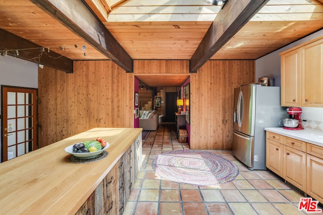 kitchen featuring beam ceiling, wooden walls, stainless steel fridge with ice dispenser, wooden ceiling, and light brown cabinets