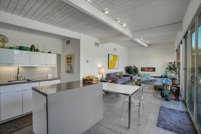 kitchen featuring sink, beam ceiling, tasteful backsplash, white cabinets, and a kitchen island