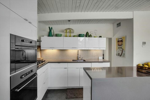 kitchen with sink, vaulted ceiling with beams, white cabinetry, stainless steel gas stovetop, and decorative backsplash