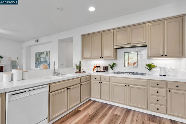 kitchen with sink, gas stovetop, tile countertops, light hardwood / wood-style flooring, and white dishwasher