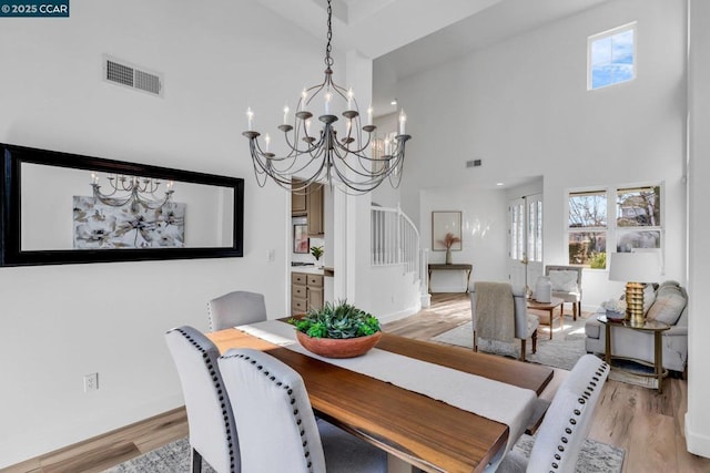 dining area with a towering ceiling, light hardwood / wood-style floors, and a notable chandelier