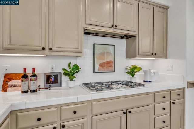 kitchen with white gas stovetop, tile counters, decorative backsplash, and cream cabinetry