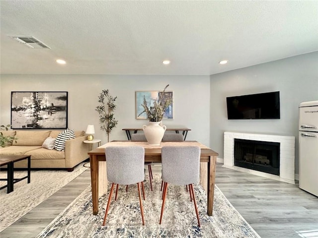 dining space with a brick fireplace, a textured ceiling, and light hardwood / wood-style flooring