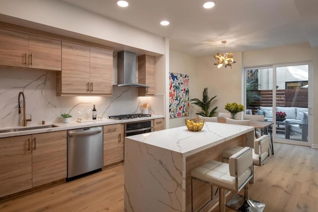 kitchen with pendant lighting, wall chimney range hood, sink, stainless steel appliances, and a kitchen island