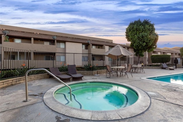 pool at dusk with a hot tub and a patio area