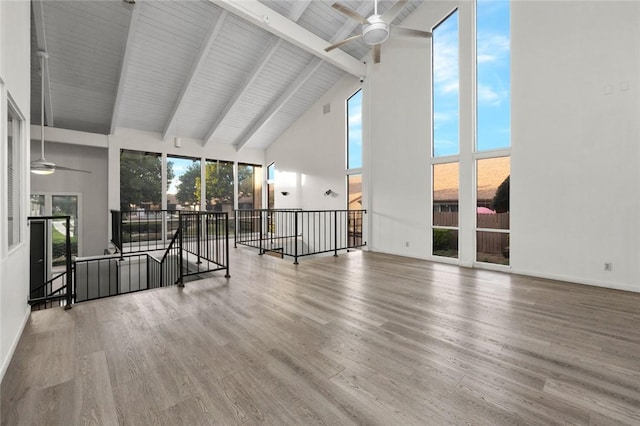 unfurnished living room featuring a healthy amount of sunlight, hardwood / wood-style floors, beam ceiling, and ceiling fan