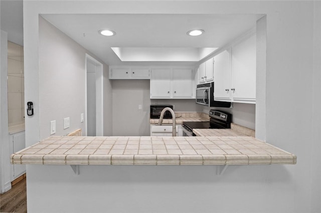 kitchen with electric stove, white cabinetry, tile countertops, and kitchen peninsula