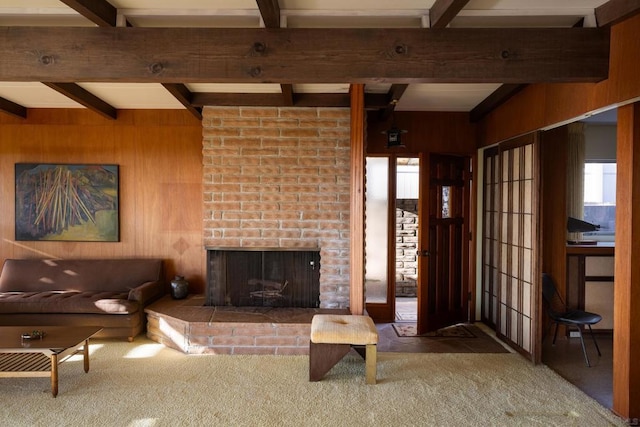 living room featuring carpet flooring, wooden walls, a brick fireplace, and beam ceiling