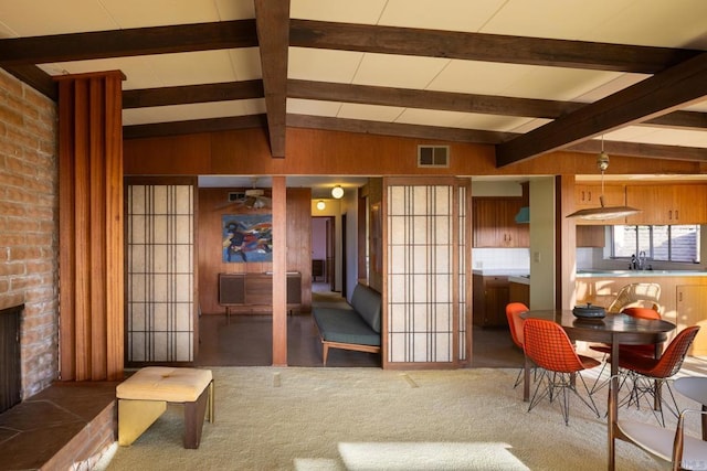 carpeted living room with sink, lofted ceiling with beams, and wood walls