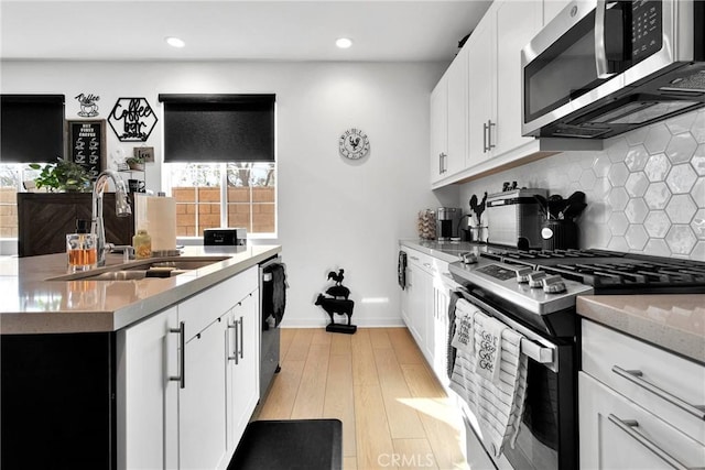 kitchen with sink, white cabinetry, light wood-type flooring, stainless steel appliances, and backsplash