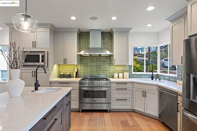 kitchen featuring appliances with stainless steel finishes, sink, wall chimney range hood, and light stone counters