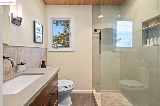 bathroom featuring vanity, a tile shower, tile walls, and toilet