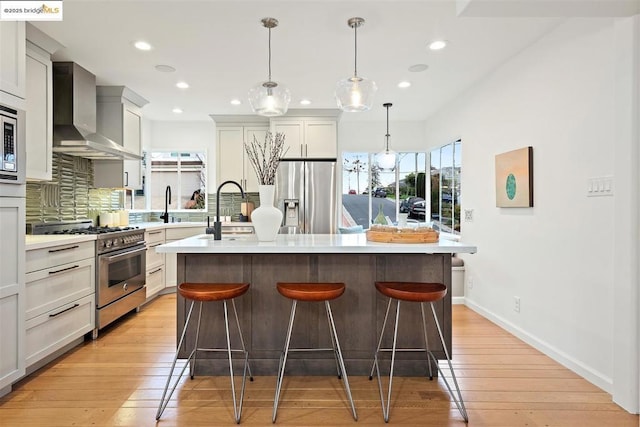 kitchen featuring stainless steel appliances, a kitchen island with sink, decorative backsplash, and wall chimney range hood