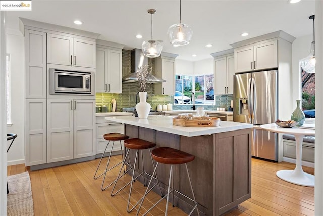 kitchen with wall chimney range hood, a breakfast bar, stainless steel appliances, a center island, and decorative light fixtures