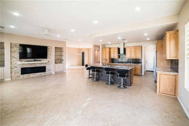 kitchen with light stone counters, wall chimney exhaust hood, a kitchen bar, and a kitchen island with sink