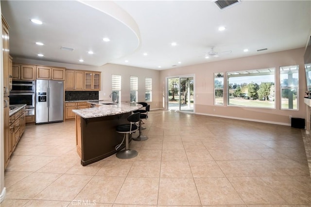 kitchen with appliances with stainless steel finishes, backsplash, a kitchen bar, a large island with sink, and light stone counters