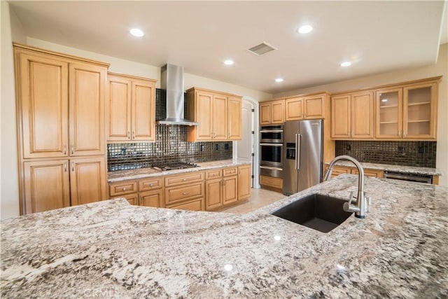 kitchen featuring wall chimney range hood, sink, appliances with stainless steel finishes, backsplash, and light stone counters