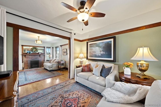 living room featuring ceiling fan, hardwood / wood-style floors, and a brick fireplace