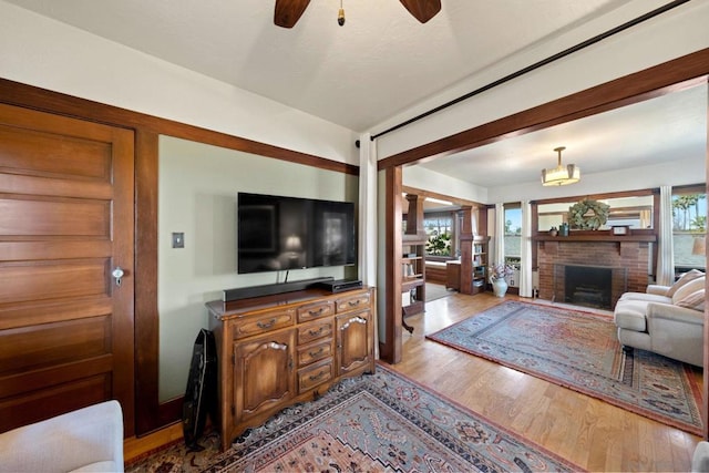 living room featuring a brick fireplace, a wealth of natural light, ceiling fan, and light wood-type flooring