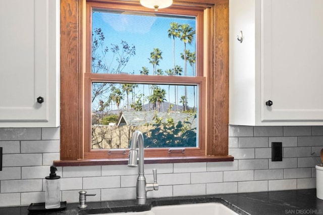 details with tasteful backsplash, white cabinetry, sink, and dark stone countertops