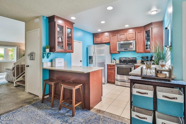 kitchen with light tile patterned floors, a breakfast bar area, stainless steel appliances, light stone counters, and kitchen peninsula