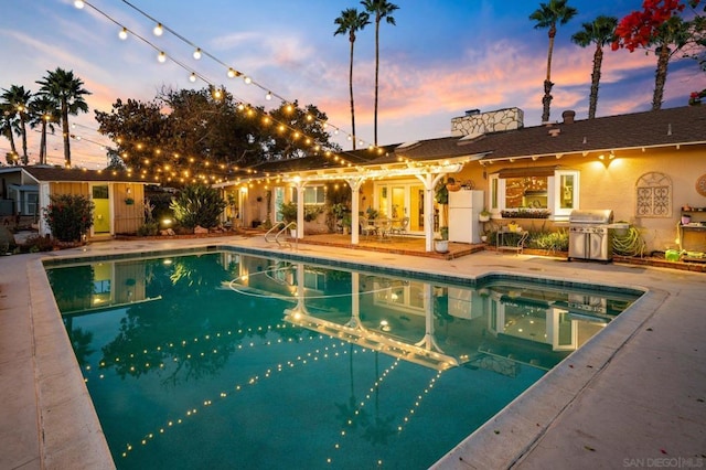 pool at dusk with area for grilling and a patio area