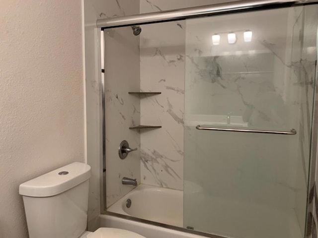 bathroom featuring toilet and bath / shower combo with glass door