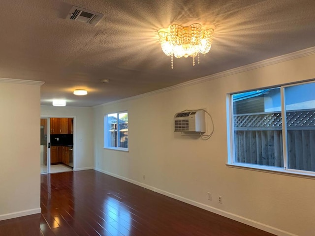 empty room featuring dark wood-type flooring, a wall mounted air conditioner, ornamental molding, a textured ceiling, and a chandelier