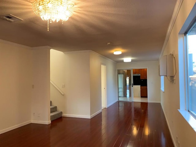 unfurnished room with a notable chandelier, crown molding, dark wood-type flooring, and a textured ceiling