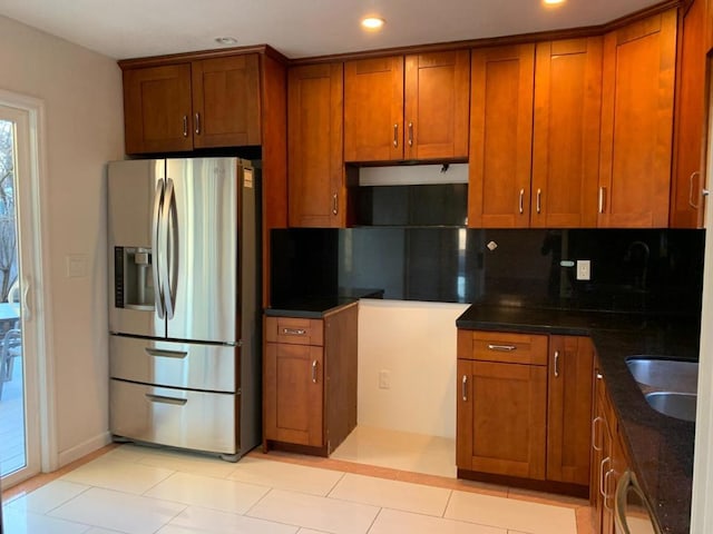 kitchen featuring sink, light tile patterned floors, stainless steel fridge, backsplash, and dark stone counters