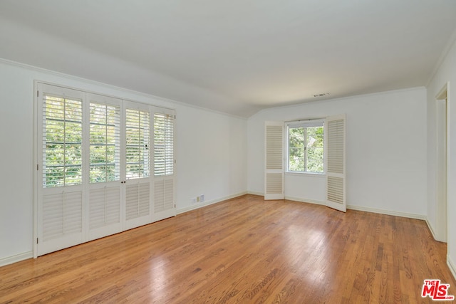 empty room with ornamental molding, light hardwood / wood-style floors, and vaulted ceiling