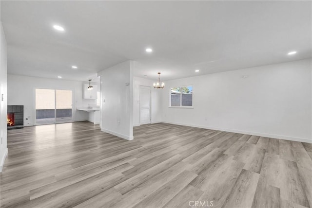 unfurnished living room featuring an inviting chandelier and light hardwood / wood-style floors