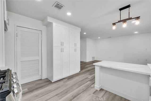 kitchen featuring light wood-type flooring, pendant lighting, white cabinets, and light stone counters