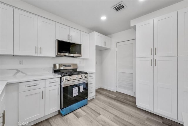 kitchen with white cabinetry, appliances with stainless steel finishes, light stone counters, and light wood-type flooring