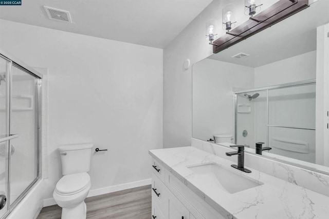 full bathroom with hardwood / wood-style flooring, enclosed tub / shower combo, vanity, and toilet