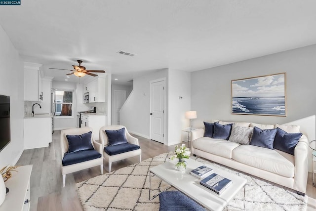 living room with ceiling fan, sink, and light wood-type flooring