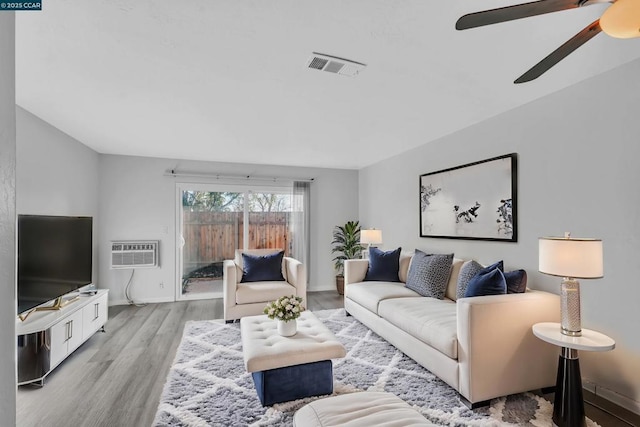 living room featuring a wall mounted air conditioner, ceiling fan, and light hardwood / wood-style flooring