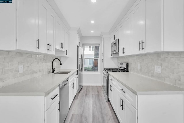 kitchen featuring sink, light hardwood / wood-style flooring, white cabinets, stainless steel appliances, and backsplash